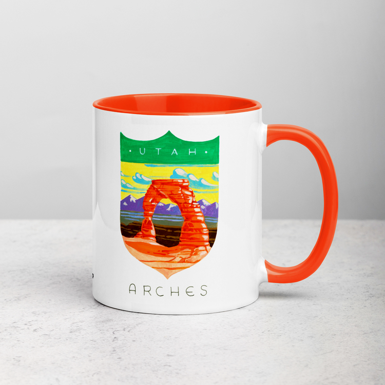 White ceramic coffee mug with orange handle and inside; has Arches National Park illustration by Angela Staehling