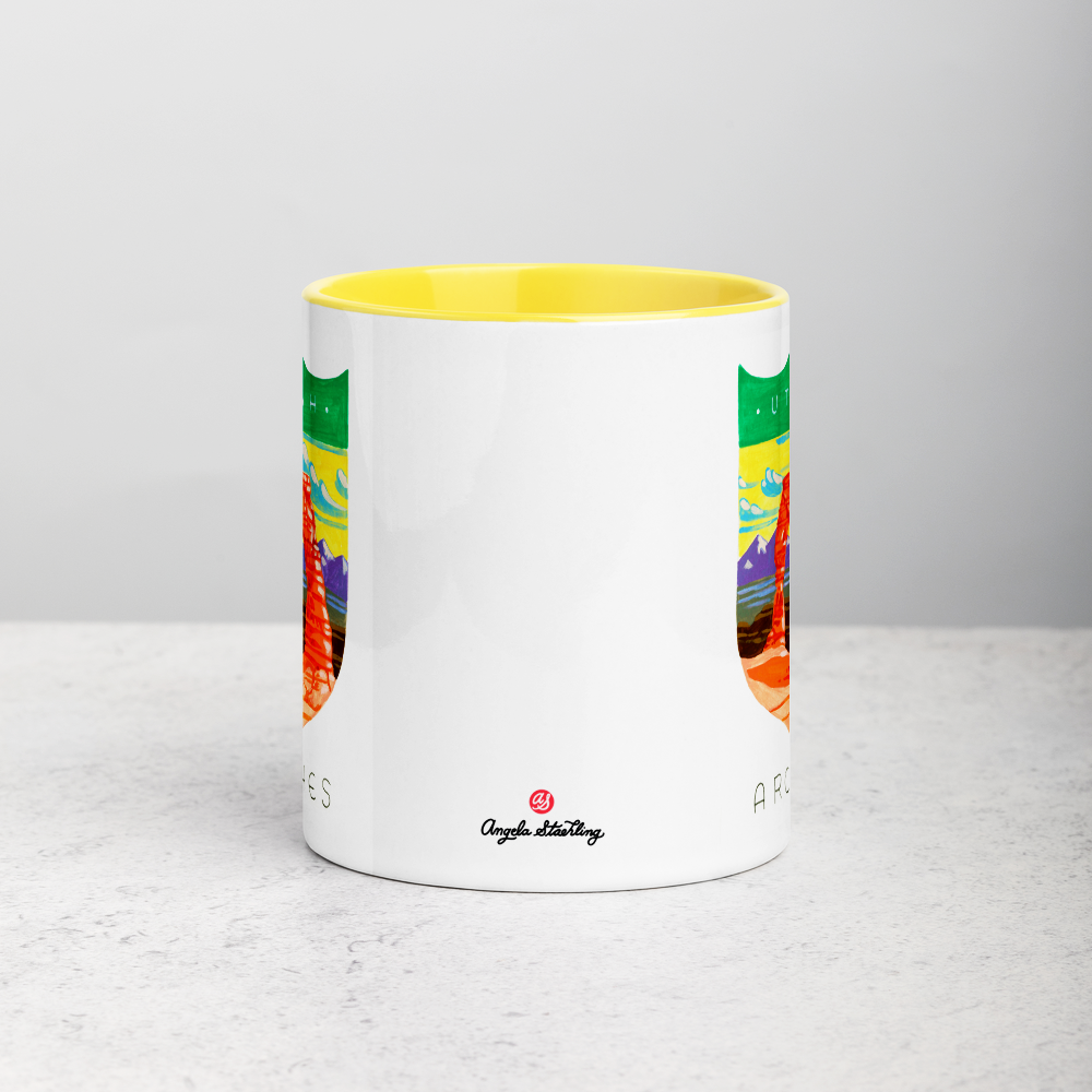 White ceramic coffee mug with yellow handle and inside; has Arches National Park illustration by Angela Staehling