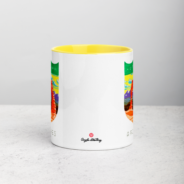 White ceramic coffee mug with yellow handle and inside; has Arches National Park illustration by Angela Staehling