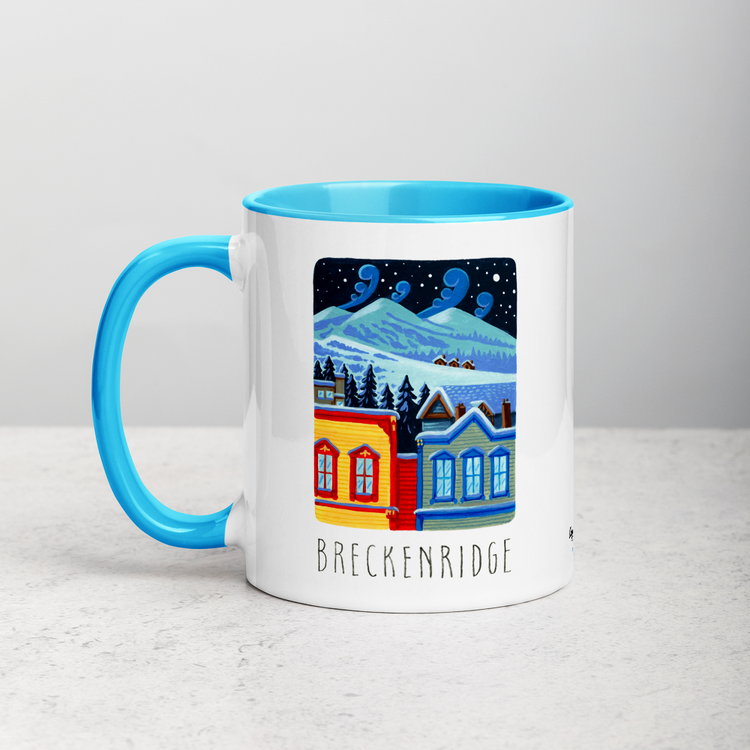 White ceramic coffee mug with blue handle and inside; has Breckenridge illustration by Angela Staehling