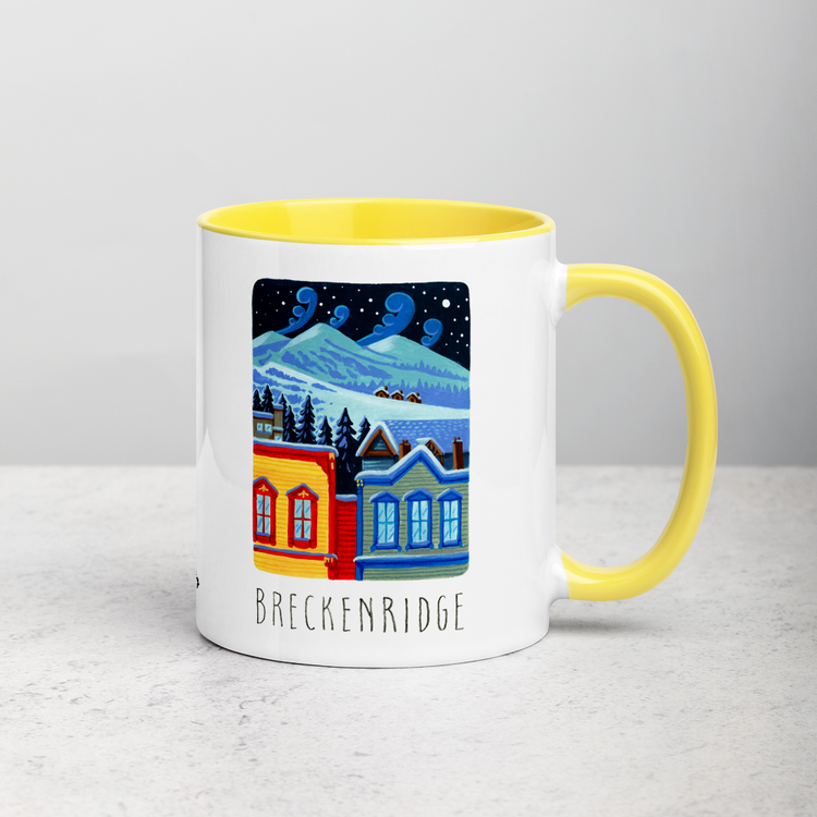 White ceramic coffee mug with yellow handle and inside; has Breckenridge illustration by Angela Staehling