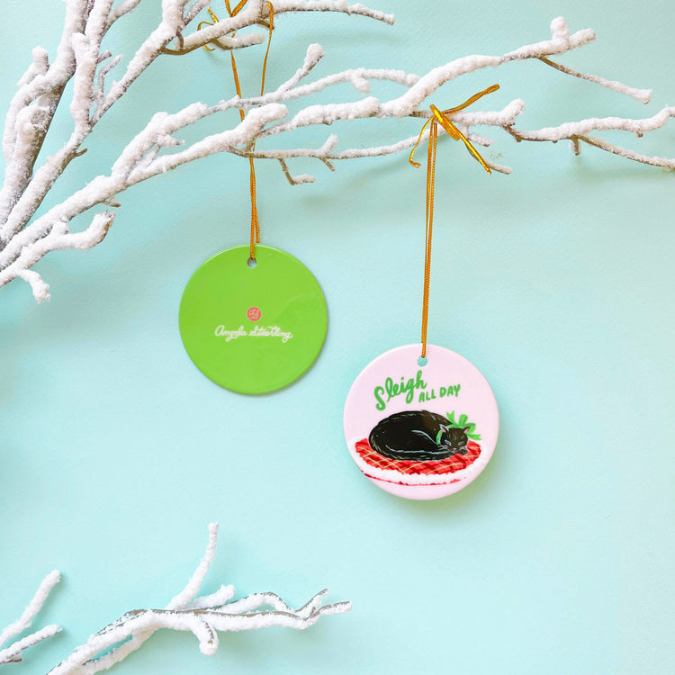 Black cat porcelain Christmas ornament wearing Christmas ribbon hanging from snowy branch