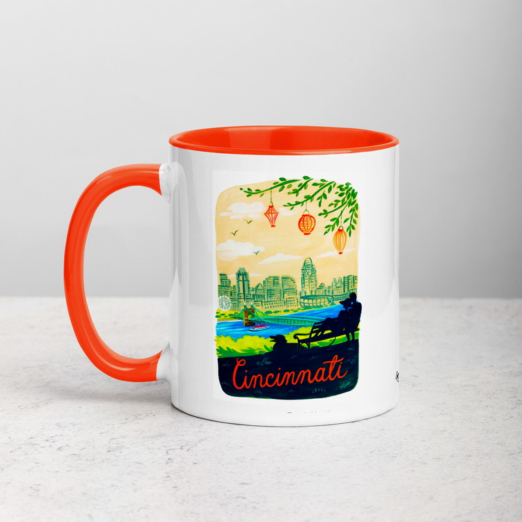 White ceramic coffee mug with orange handle and inside; has Cincinnati Ohio illustration by Angela Staehling
