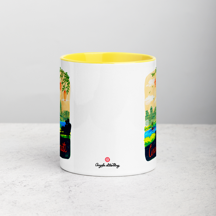 White ceramic coffee mug with yellow handle and inside; has Cincinnati Ohio illustration by Angela Staehling