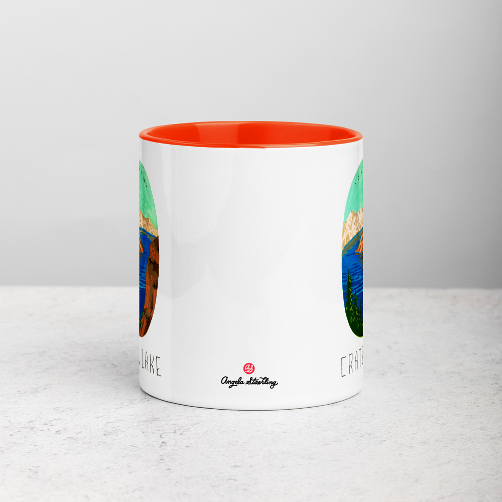 White ceramic coffee mug with orange handle and inside; has Crater Lake National Park illustration by Angela Staehling