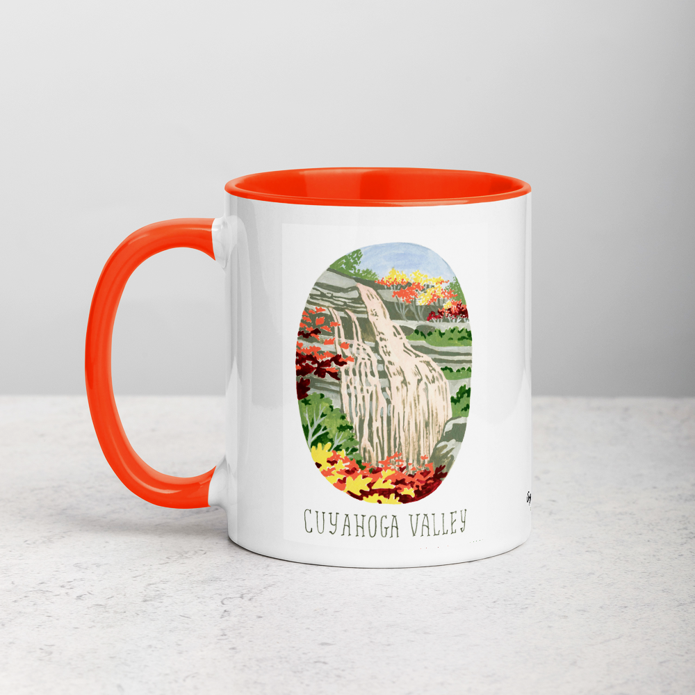 White ceramic coffee mug with orange handle and inside; has Cuyahoga Valley National Park illustration by Angela Staehling