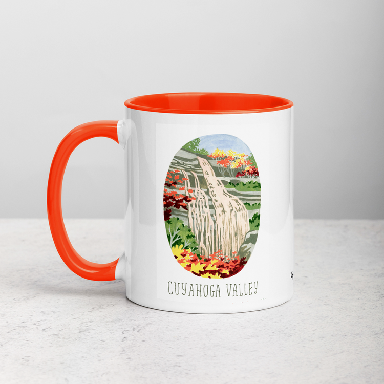 White ceramic coffee mug with orange handle and inside; has Cuyahoga Valley National Park illustration by Angela Staehling
