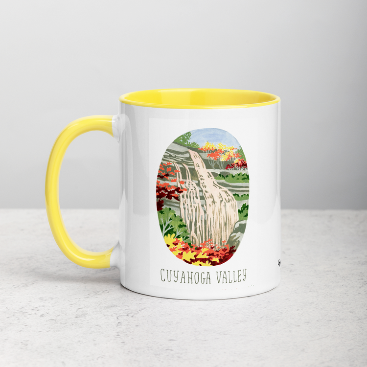 White ceramic coffee mug with yellow handle and inside; has Cuyahoga Valley National Park illustration by Angela Staehling