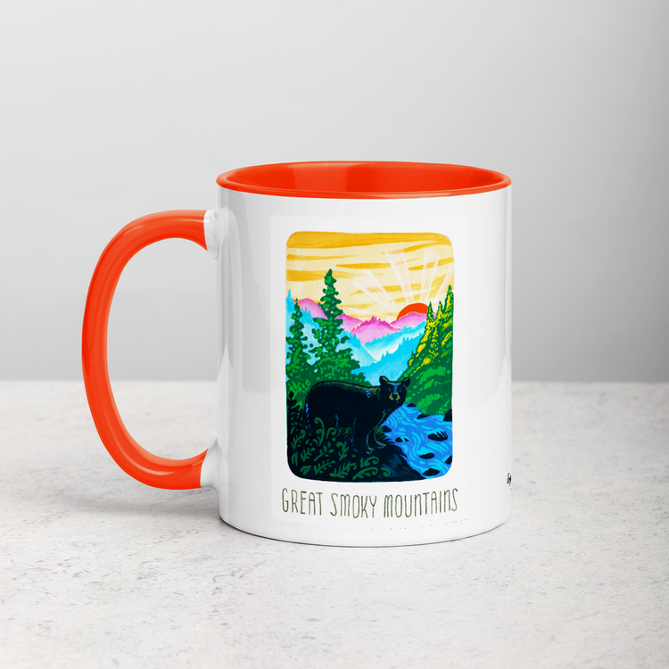 White ceramic coffee mug with orange handle and inside; has Great Smoky Mountains National Park illustration by Angela Staehling