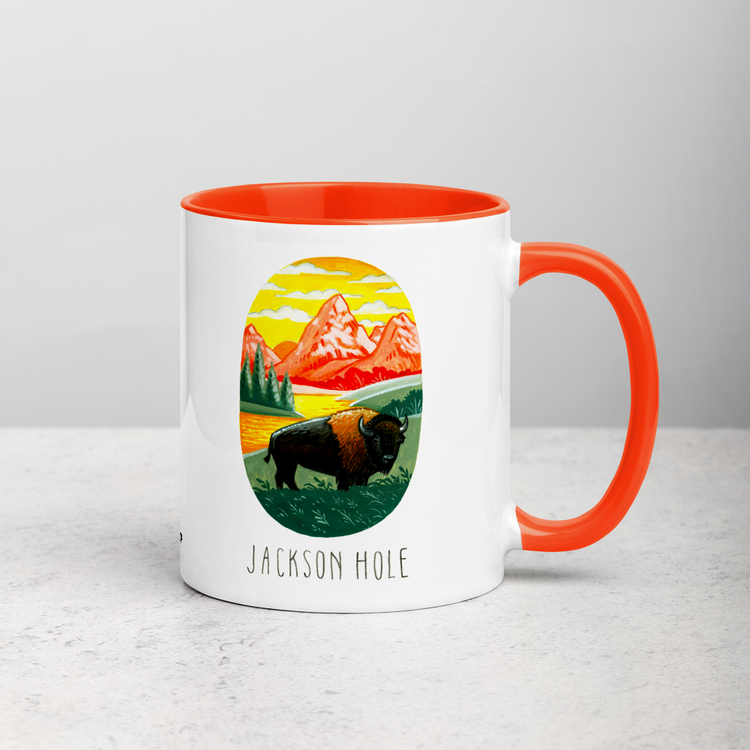 White ceramic coffee mug with orange handle and inside; has Jackson Hole National Park illustration by Angela Staehling