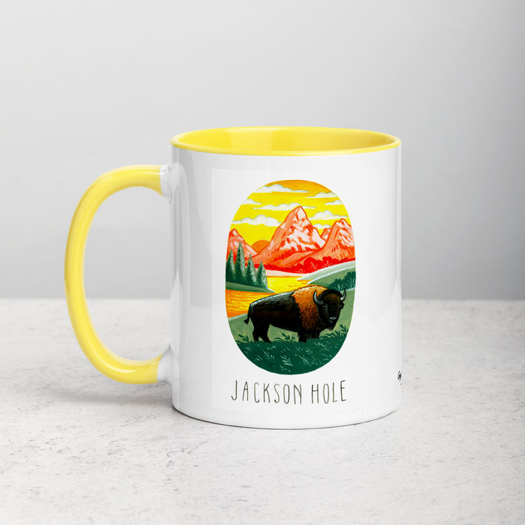White ceramic coffee mug with yellow handle and inside; has Jackson Hole National Park illustration by Angela Staehling