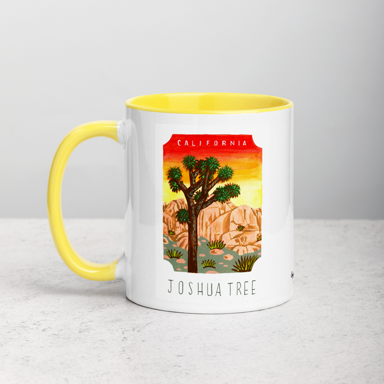 White ceramic coffee mug with yellow handle and inside; has Joshua Tree National Park illustration by Angela Staehling