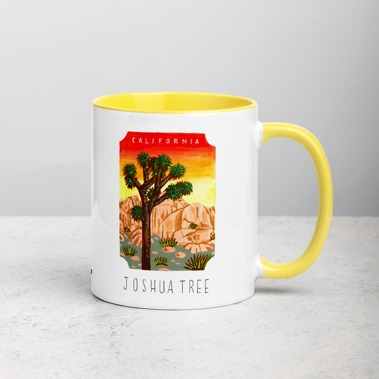 White ceramic coffee mug with yellow handle and inside; has Joshua Tree National Park illustration by Angela Staehling