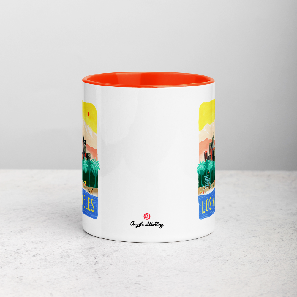 White ceramic coffee mug with orange handle and inside; has Los Angeles California illustration by Angela Staehling