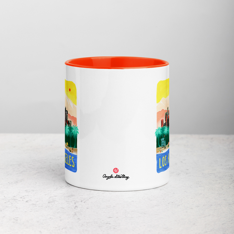 White ceramic coffee mug with orange handle and inside; has Los Angeles California illustration by Angela Staehling
