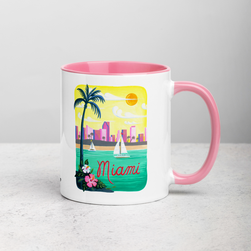 White ceramic coffee mug with pink handle and inside; has Miami Florida illustration by Angela Staehling
