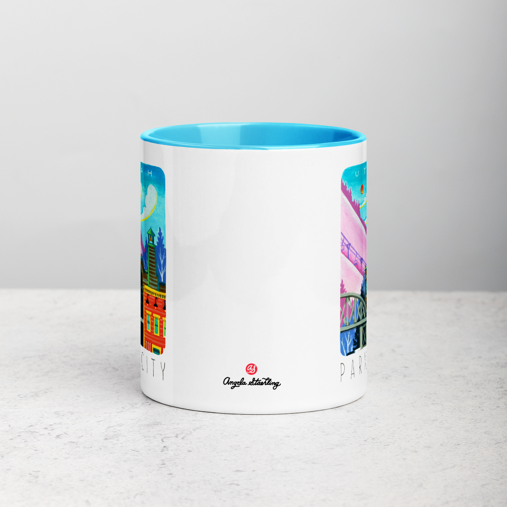 White ceramic coffee mug with blue handle and inside; has Park City illustration by Angela Staehling