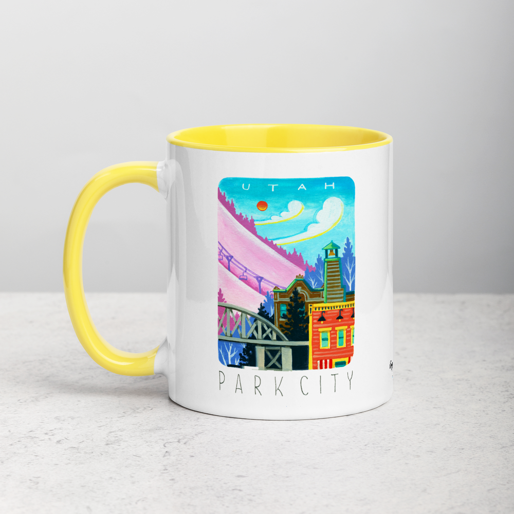 White ceramic coffee mug with yellow handle and inside; has Park City illustration by Angela Staehling