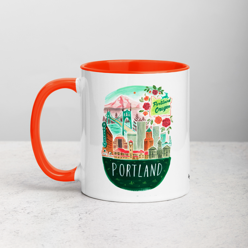 White ceramic coffee mug with orange handle and inside; has Portland Oregon illustration by Angela Staehling