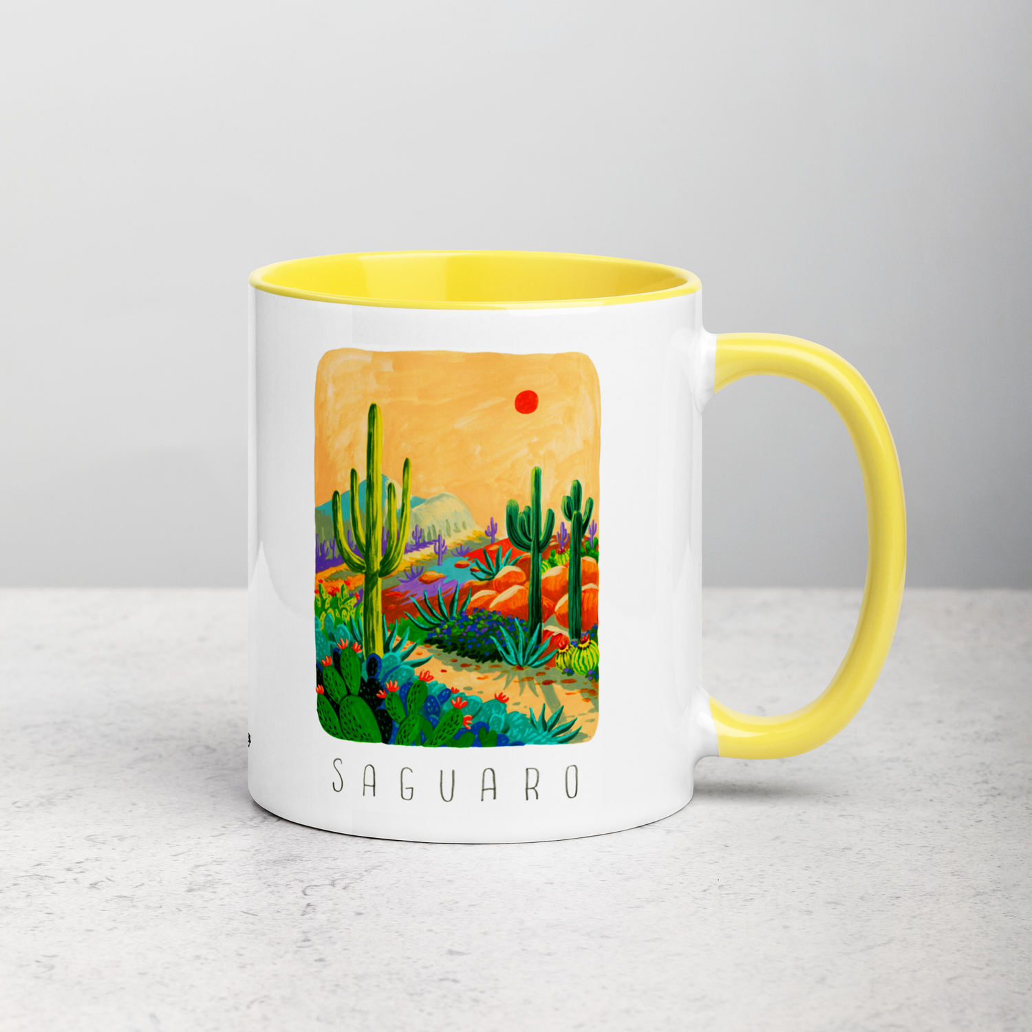 White ceramic coffee mug with yellow handle and inside; has Saguaro National Park illustration by Angela Staehling