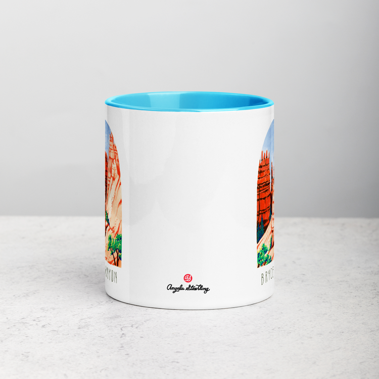 White ceramic coffee mug with blue handle and inside; has Bryce Canyon art by Angela Staehling