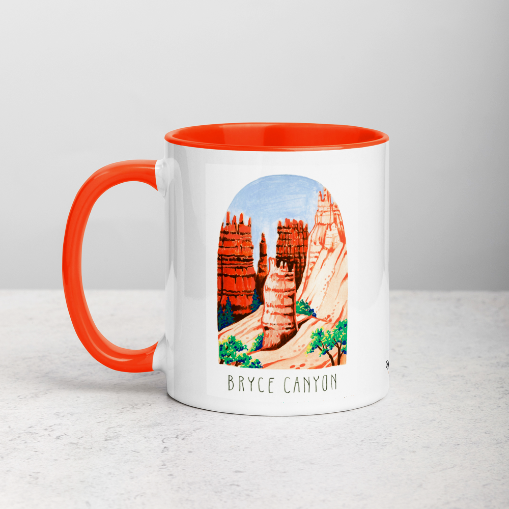White ceramic coffee mug with orange handle and inside; has Bryce Canyon art by Angela Staehling