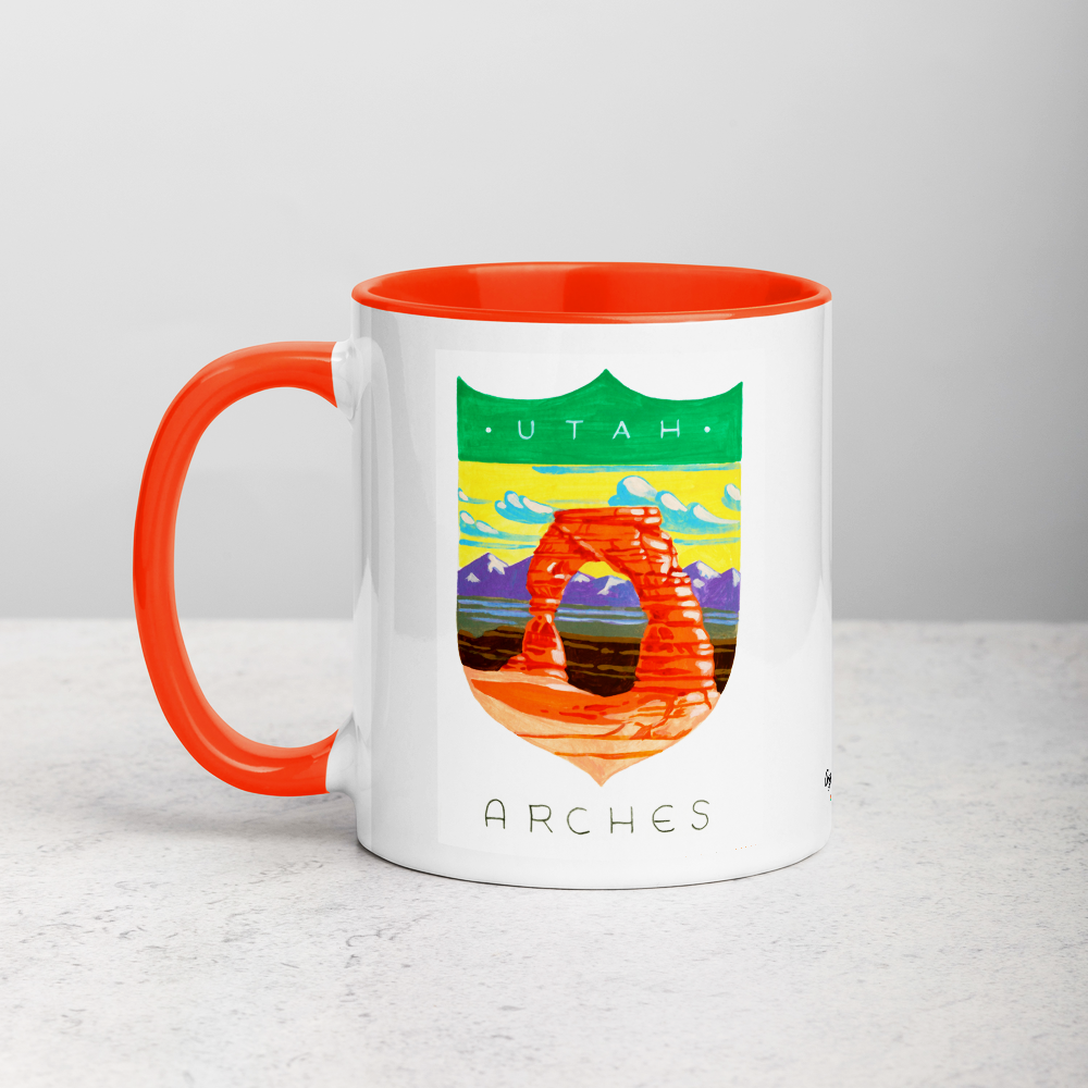 White ceramic coffee mug with orange handle and inside; has Arches National Park illustration by Angela Staehling