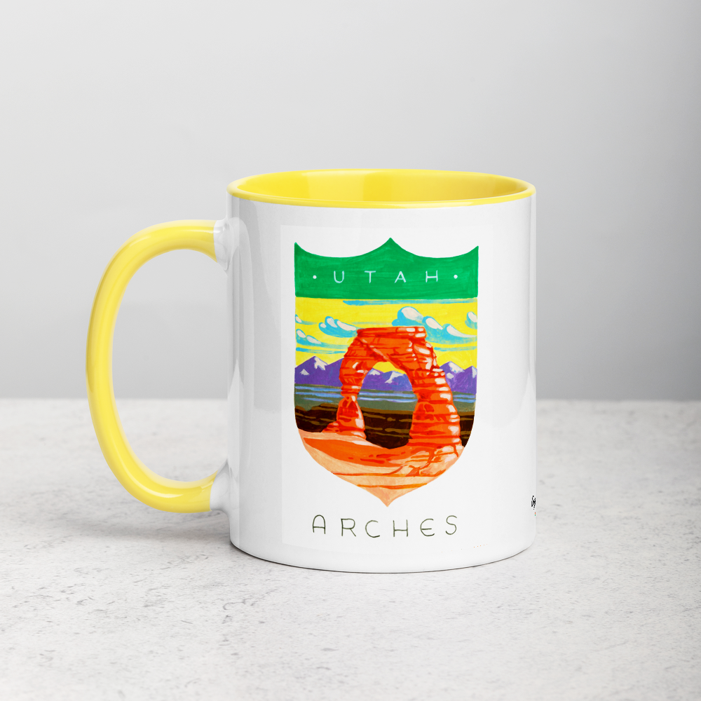 White ceramic coffee mug with yellow handle and inside; has Arches National Park illustration by Angela Staehling