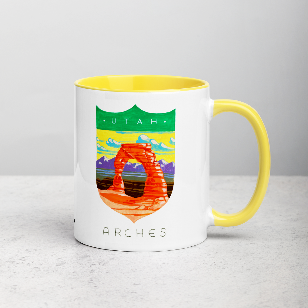 White ceramic coffee mug with yellow handle and inside; has Arches National Park illustration by Angela Staehling