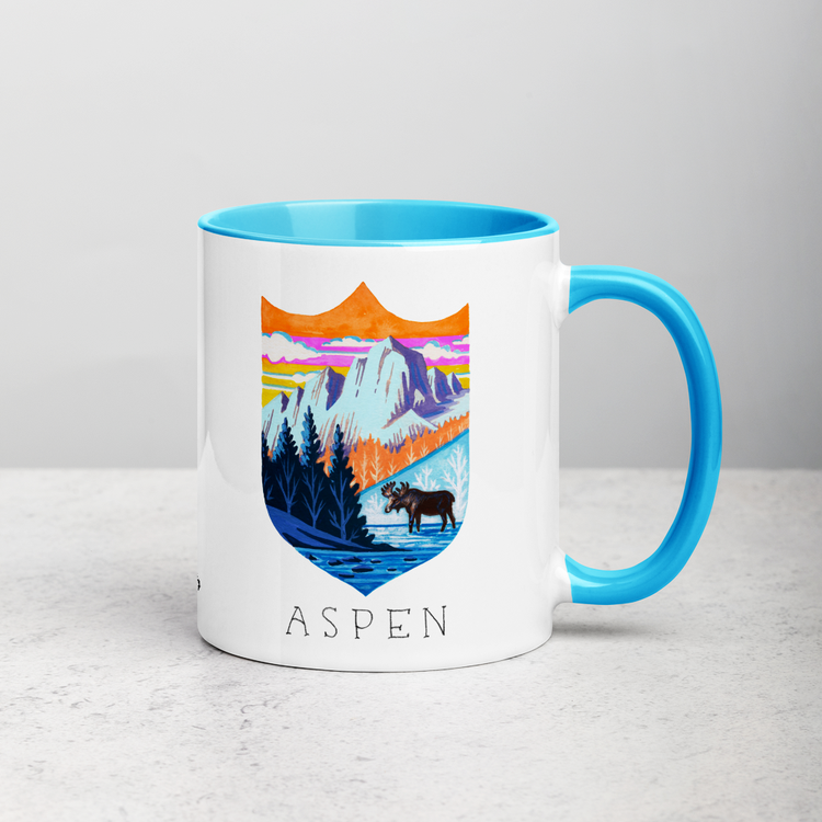 White ceramic coffee mug with blue handle and inside; has Aspen Colorado illustration by Angela Staehling