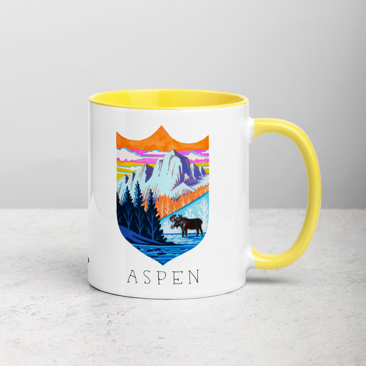 White ceramic coffee mug with yellow handle and inside; has Aspen Colorado illustration by Angela Staehling