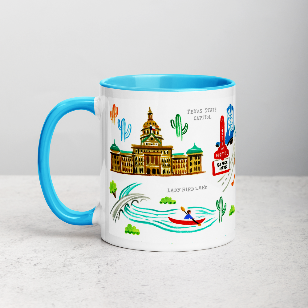White ceramic coffee mug with blue handle and inside; has Austin landmarks illustration by Angela Staehling