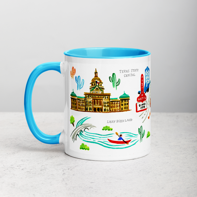 White ceramic coffee mug with blue handle and inside; has Austin landmarks illustration by Angela Staehling