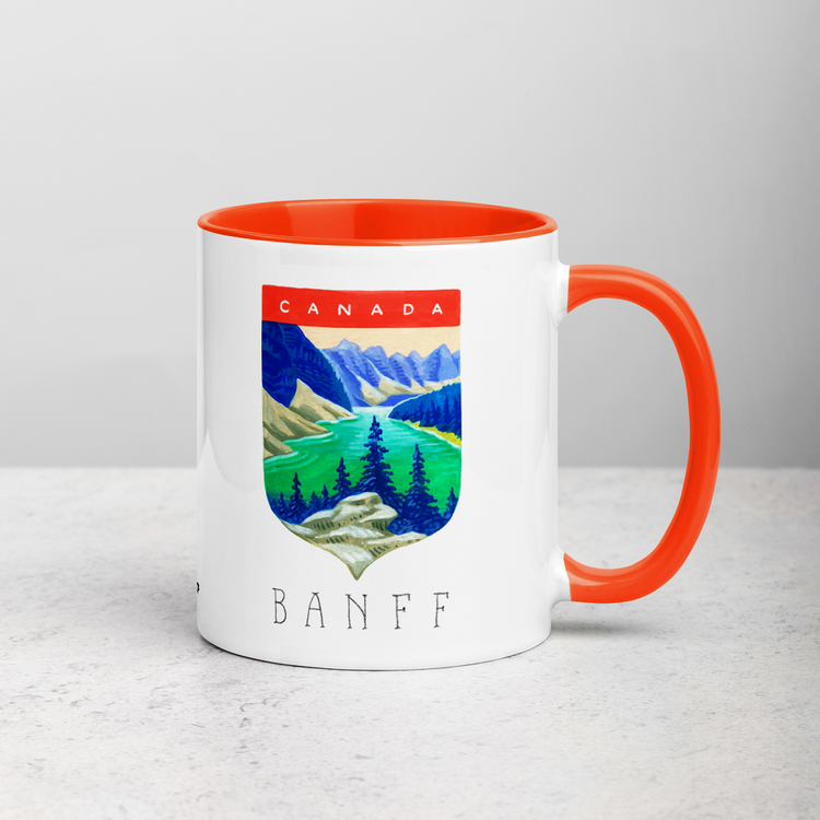White ceramic coffee mug with orange handle and inside; has Banff National Park illustration by Angela Staehling