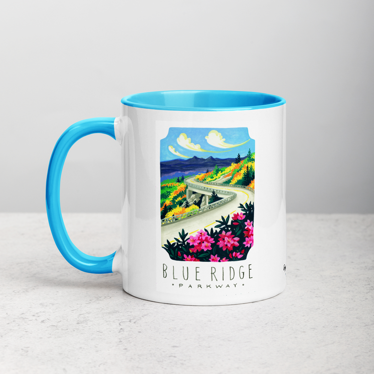 White ceramic coffee mug with blue handle and inside; has Blue Ridge Parkway National Park illustration by Angela Staehling