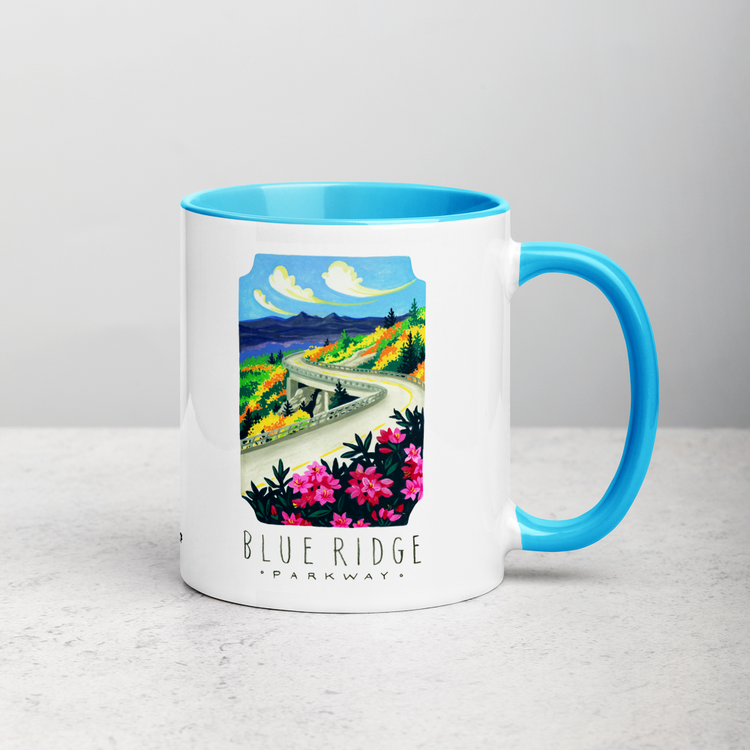 White ceramic coffee mug with blue handle and inside; has Blue Ridge Parkway National Park illustration by Angela Staehling