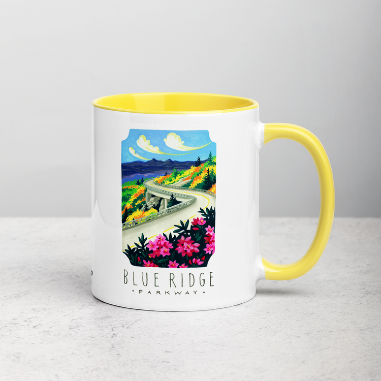 White ceramic coffee mug with yellow handle and inside; has Blue Ridge Parkway National Park illustration by Angela Staehling