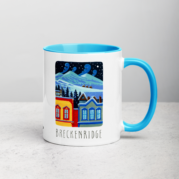 White ceramic coffee mug with blue handle and inside; has Breckenridge illustration by Angela Staehling