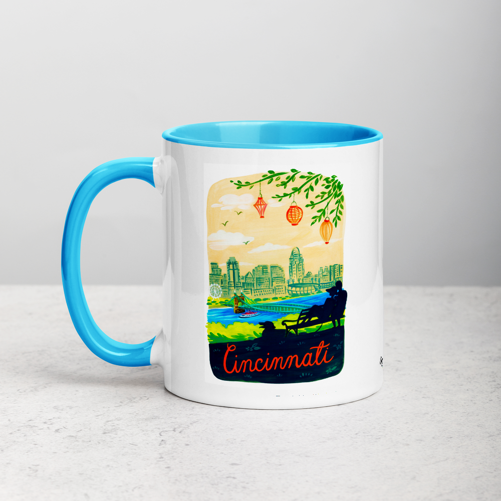 White ceramic coffee mug with blue handle and inside; has Cincinnati Ohio illustration by Angela Staehling