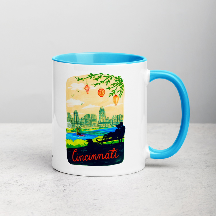 White ceramic coffee mug with blue handle and inside; has Cincinnati Ohio illustration by Angela Staehling