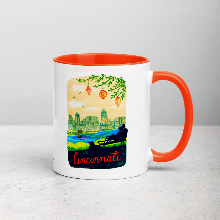White ceramic coffee mug with orange handle and inside; has Cincinnati Ohio illustration by Angela Staehling