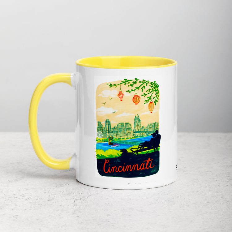 White ceramic coffee mug with yellow handle and inside; has Cincinnati Ohio illustration by Angela Staehling