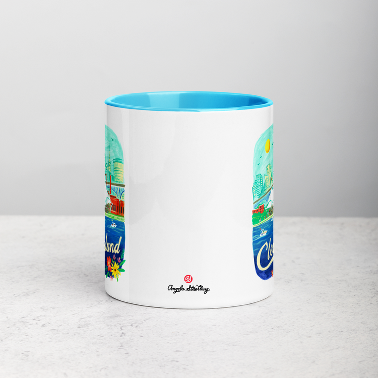 White ceramic coffee mug with blue handle and inside; has Cleveland Ohio illustration by Angela Staehling
