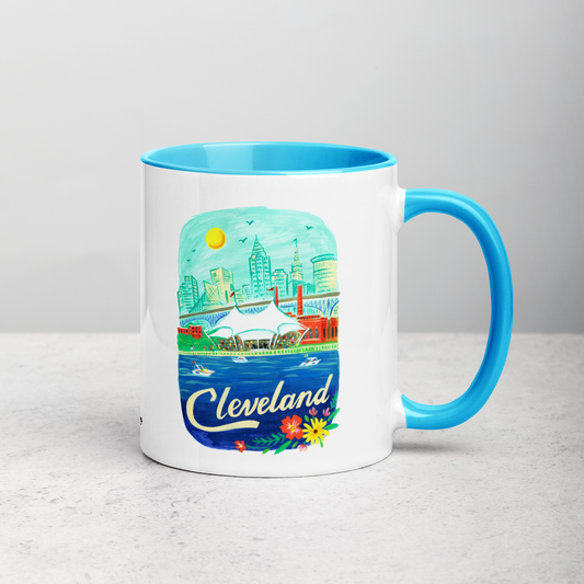White ceramic coffee mug with blue handle and inside; has Cleveland Ohio illustration by Angela Staehling