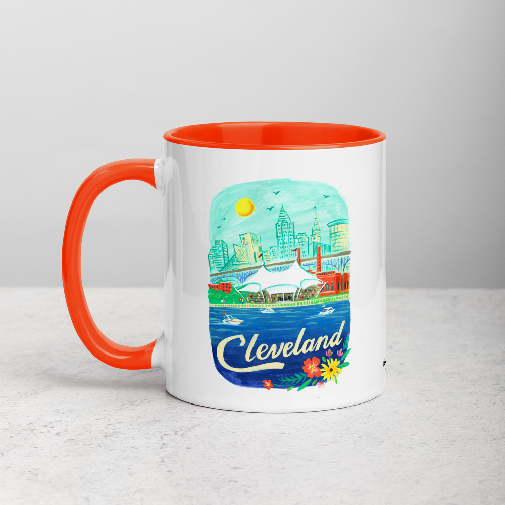 White ceramic coffee mug with orange handle and inside; has Cleveland Ohio illustration by Angela Staehling