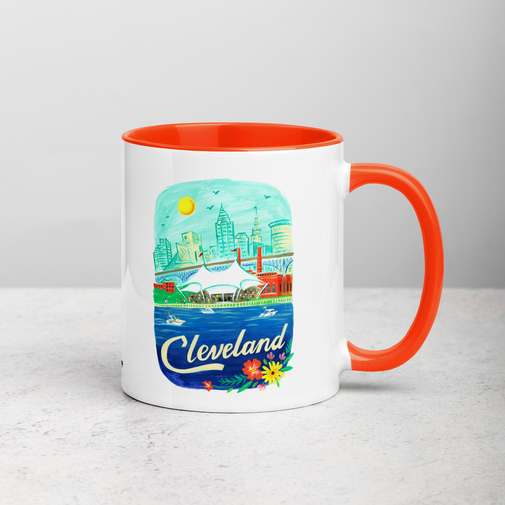 White ceramic coffee mug with orange handle and inside; has Cleveland Ohio illustration by Angela Staehling