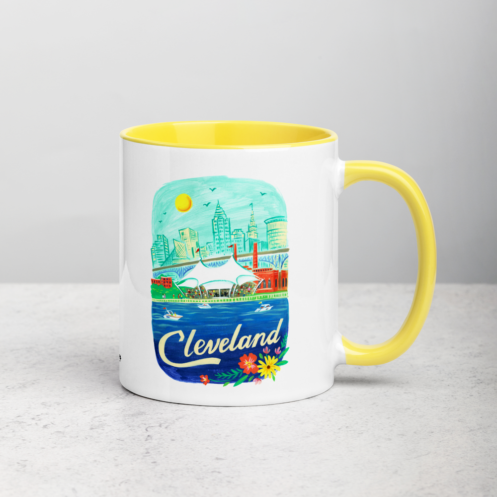 White ceramic coffee mug with yellow handle and inside; has Cleveland Ohio illustration by Angela Staehling