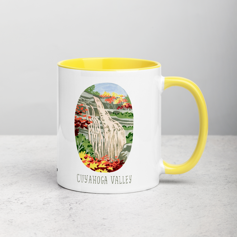White ceramic coffee mug with yellow handle and inside; has Cuyahoga Valley National Park illustration by Angela Staehling