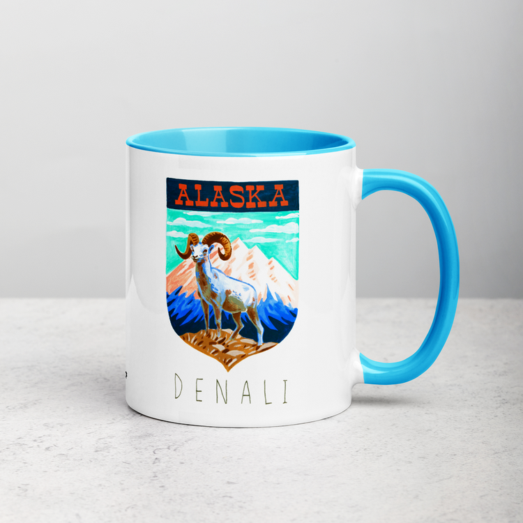 White ceramic coffee mug with blue handle and inside; has Denali National Park illustration by Angela Staehling