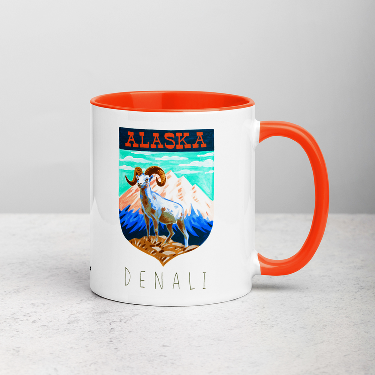 White ceramic coffee mug with orange handle and inside; has Denali National Park illustration by Angela Staehling